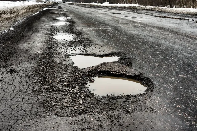 Severe pothole on a salted Syracuse city street during winter thaw